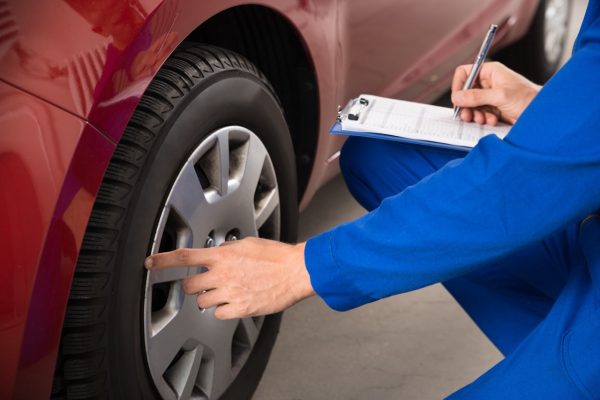 Young Mechanic Writing On Clipboard White Examining Car Wheel