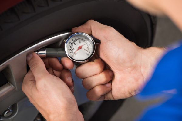 Close-up Of Mechanic Checking Air Pressure Level In Car Tire